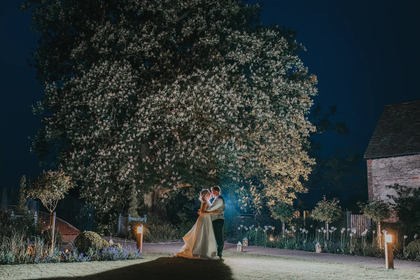 bride and groom by a tree in the garden at night