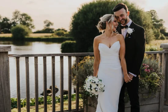 Bride and groom stand lakeside on their wedding day at this barn wedding venue in Cheshire