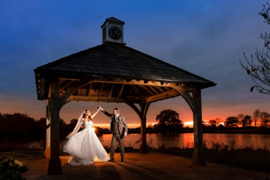 A couple dance under the Clock Tower by the lake at Sandhole Oak Barn wedding venue in Cheshire