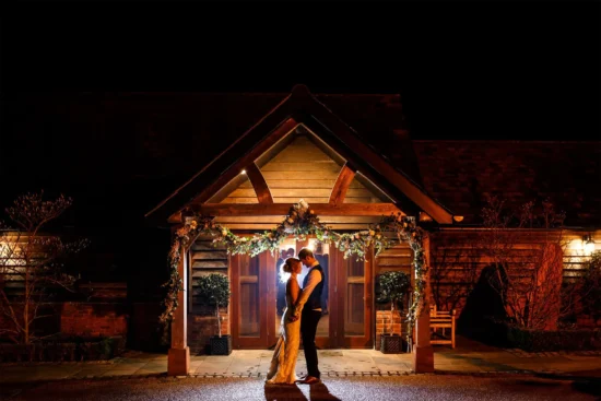A couple kiss outside the oak barn during their evening reception at Sandhole Oak Barn